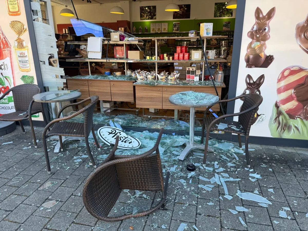 Man sieht eine zerstörte Scheibe und umgefallene Tische und Stühle. 